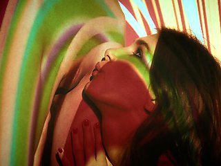 Ellie Luna and Leona Mia kiss slowly under swirling red and yellow light projections